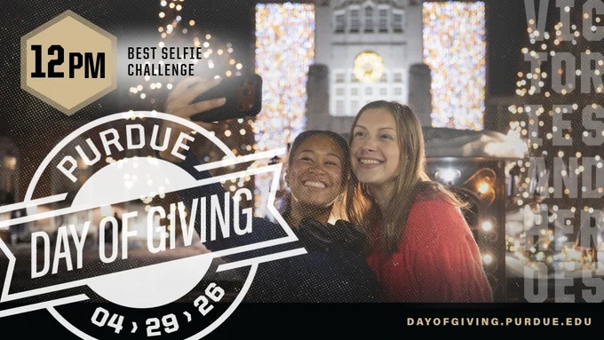 Two people taking a selfie in front of the Purdue Memorial Union holiday light display at night.