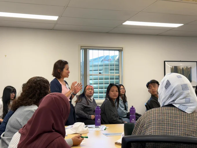 One participant standing up and sharing their insights with the group sitting around a table in the classroom.