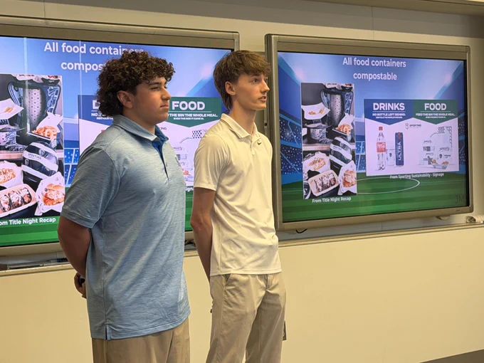 Two young men standing in front of a display about Sporting Kansas City sustainability program.