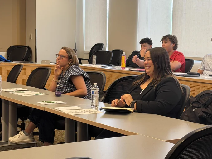 A group of people seated at tables in a classroom or meeting room, engaged in discussion or work.