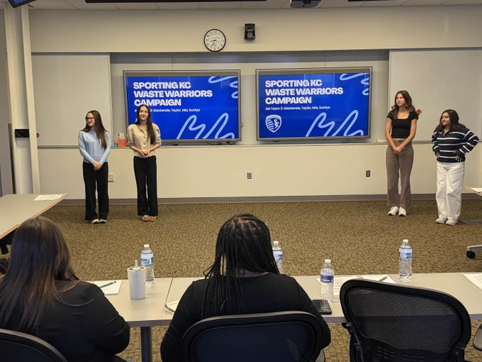 Classroom setting with several students seated at desks and Sporting KC branding on signage behind them.