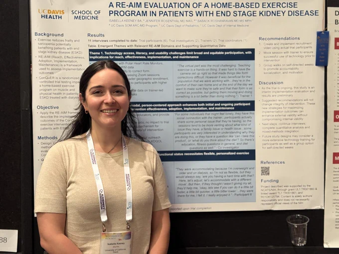 A smiling researcher stands in front of a UC Davis Health poster presentation on a home-based exercise program for patients with end stage kidney disease at a conference.