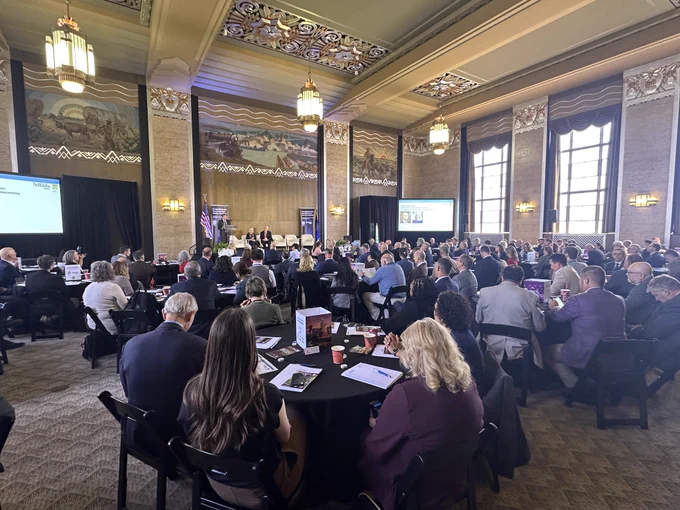 Audience seated at round tables inside a large historic hall at the Durham Museum in Omaha, listening to speakers on stage during a bioeconomy competitiveness conference.