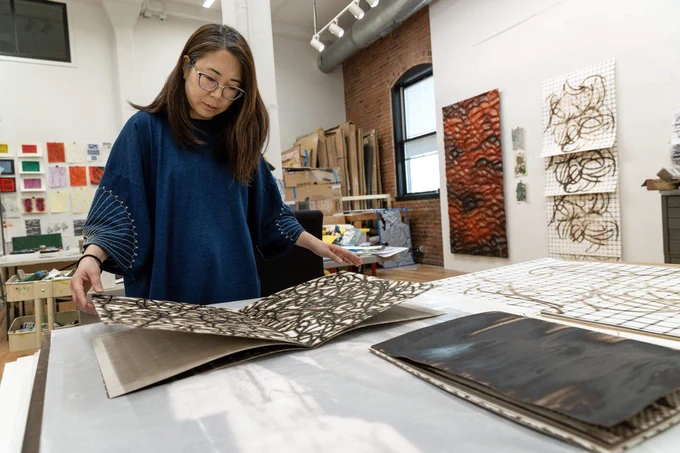 Artist Lucy Kim looks through a melanin print book at her studio in Somerville, Mass.