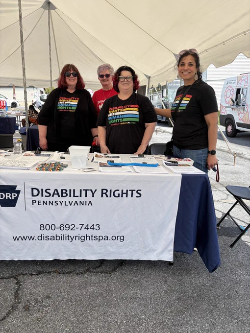 DRP Staff Reneece, Kim, Dale and the founder of Disability Pride Pa, Vicki Landers, stand behind the DRP resource table at Disability Pride Harrisburg. 