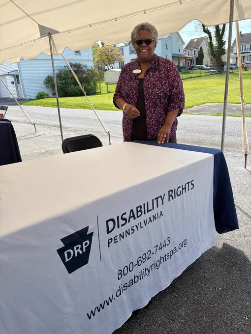 DRP Board Chair Lucy Piggott-Prawl standing behind the DRP resource table at Disability Pride Harrisburg.