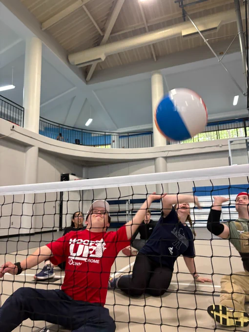 Individuals seated on a gymnasium floor playing sitting volleyball