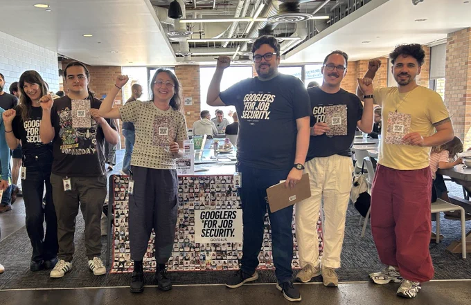 a photo of six Googlers for Job Security/AWU members in SF at work in front of a table decorated with a big collage banner of photos of Googlers for Job Security supporters, holding clipboards and flyers, and raising their fists.