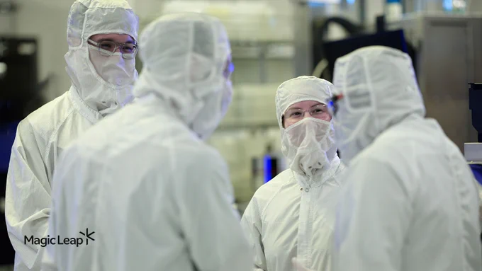 Four Magic Leap engineers in protective gear talk to each other in a room full of waveguide equipment. 