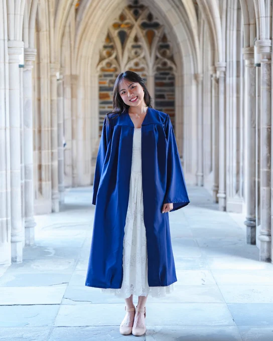 Duke student Nana Osaki in a blue graduation robe, standing and smiling in an outdoor walkway at the Duke Chapel.