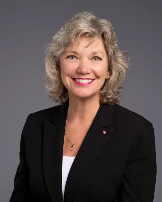 woman's headshot, black blazer, white undershirt, with blonde and gray hair smiling 