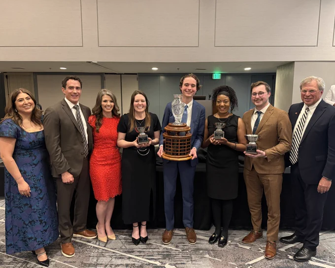 The mock trial team, coaches and TYLA judges pose for a photo. The students all hold trophies.