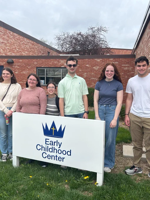 Six UI REACH students stand around a sign that says, "Early Childhood Center."