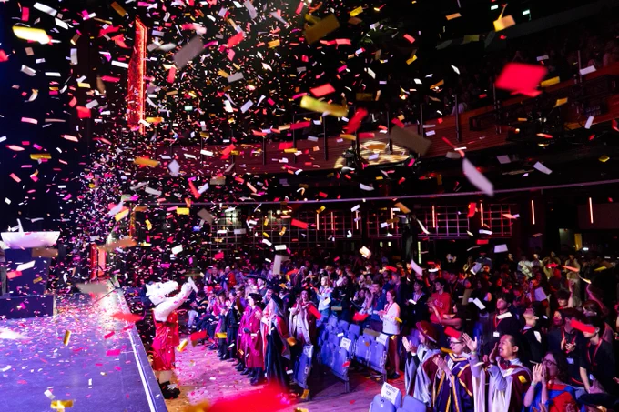 A of freshmen students and faculty showered with confetti at Convocation. In front of them, Paws, the Northeastern husky mascot \u2013 wearing red \u2013 waves and cheers.