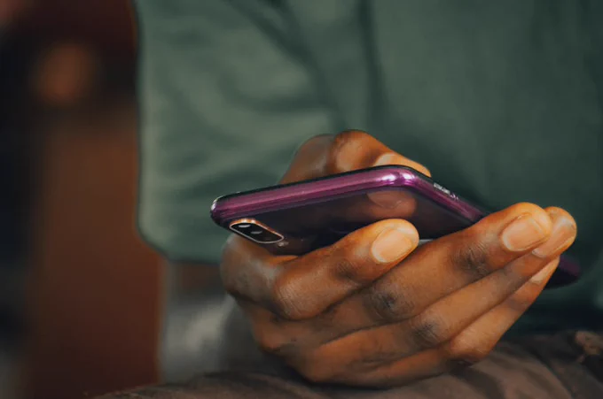 A close-up shot of a person holding a purple smartphone indoors, focusing on texting or browsing.