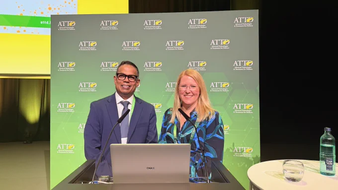 Photo of a man and woman standing side by side behind a podium. They are dressed in smart clothes and smiling towards the camera.