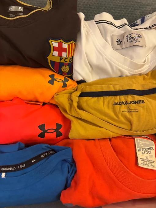 A collection of folded t-shirts featuring various logos and labels. 