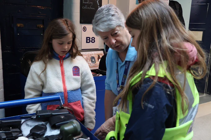 a volunteer shows items from the handling collection to two young visitors