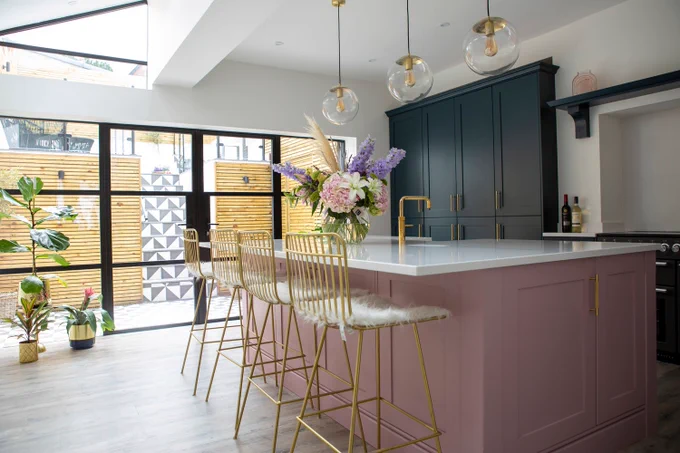 pink kitchen island with gold stools and tall dark blue cabinetry 