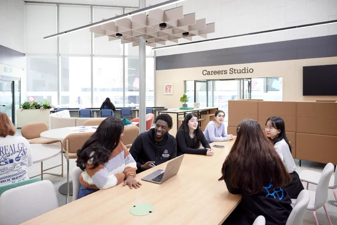 A group of students are sat in the Careers Space, chatting to each other. The Careers Studio can be seen in the background.