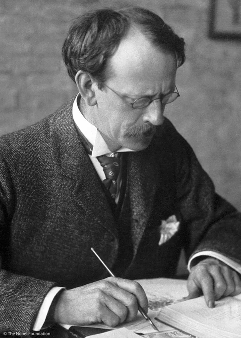 J. J. Thomson concentrating on writing in a book, dressed in a formal suit and tie.
