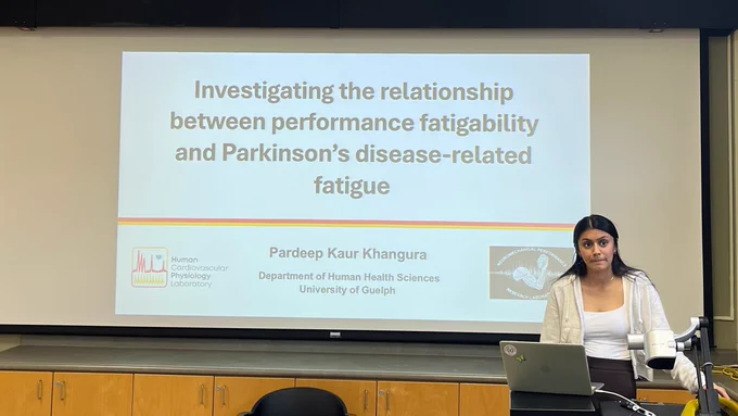 A photo of Pardeep at her defence, in front of a projected title screen with the same title of his thesis that is listed in this posting.