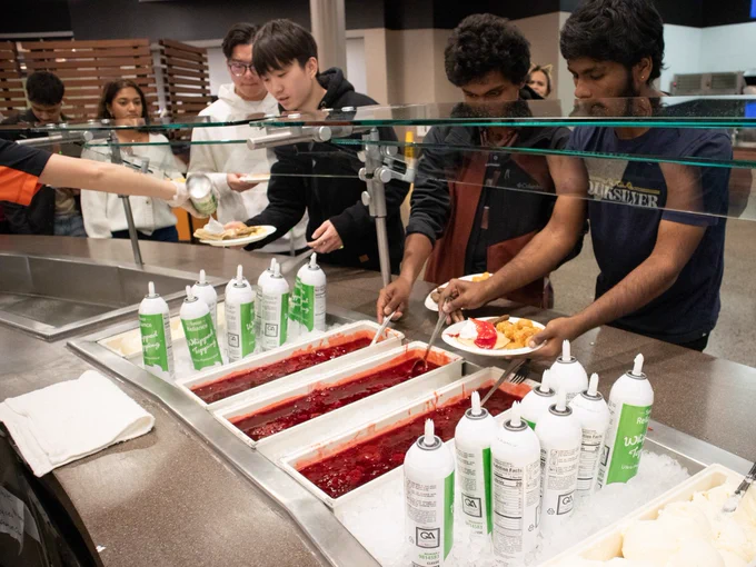 Students adding whipped cream and strawberry jam toppings for their pancakes.