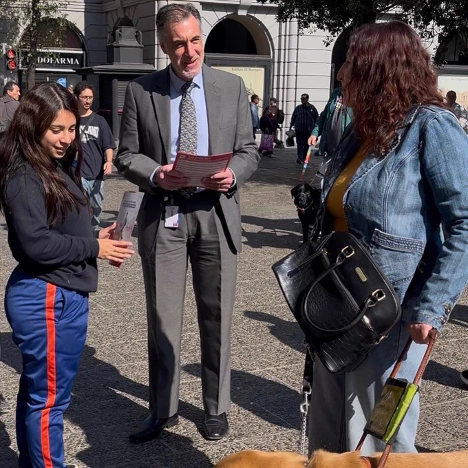 Fotografía en la que aparecen e el director nacional entregando un flyer con recomendaciones para el respeto de personas usuarias de perro guía. A su lado está Ruth Espinoza, usuaria de perro guía.