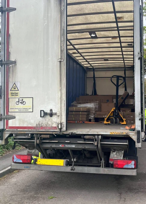 Open delivery truck with pallets and a yellow pallet jack inside, parked on a street.