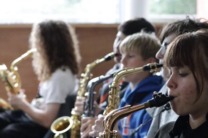 A group of young musicians seated indoors playing saxophones in a focused practice session.