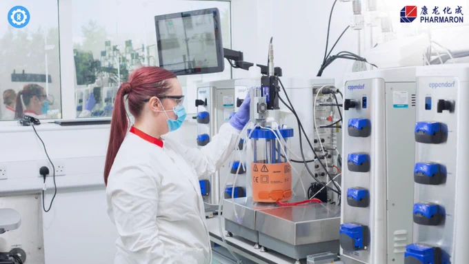 "Plasmid DNA Manufacturing for Gene Therapy Excellence. Image of a person in a white lab coat and purple gloves working with advanced biotechnological equipment, including Eppendorf bioreactors, in a sterile lab environment at Pharmaron