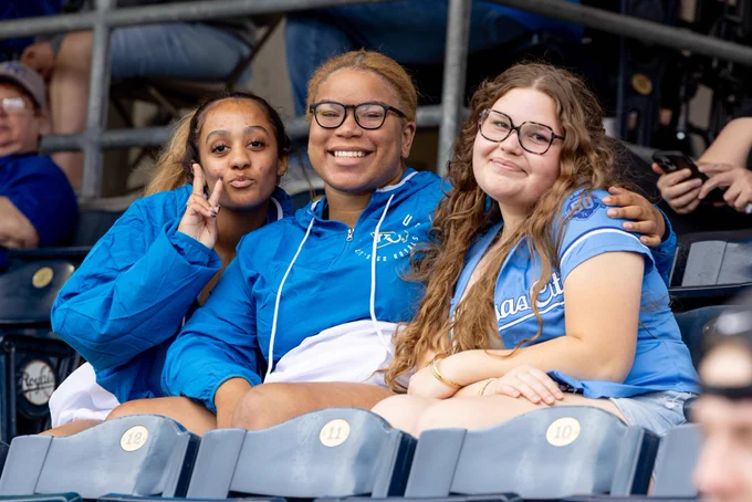 Three fans pose for a photo while sitting in Kauffman Stadium.