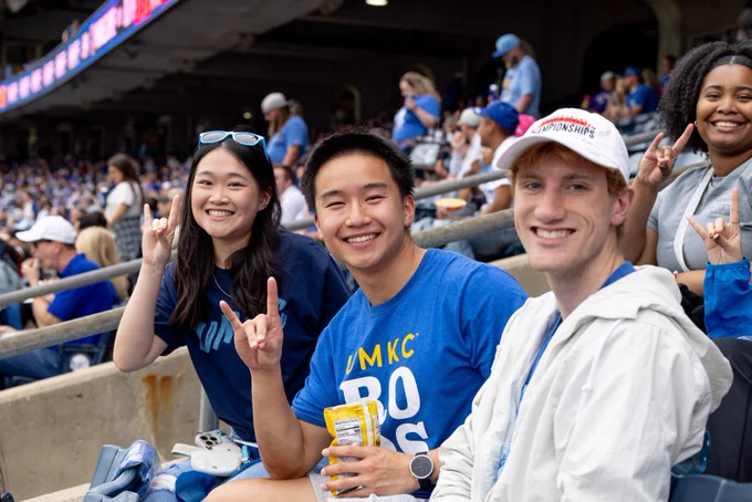 Three fans pose for a photo while sitting in the stands at a Royals game.