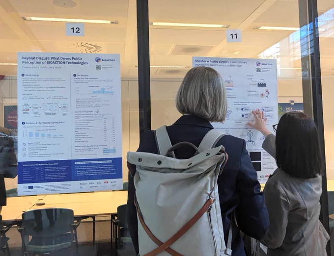 Person presenting a large scientific poster to an interested visitor.