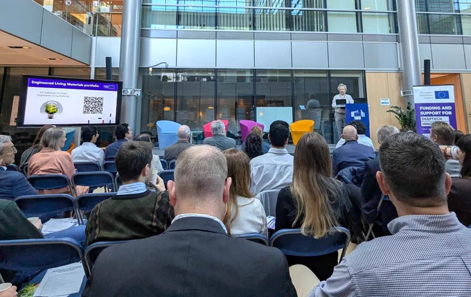 People sitting in a sunny atrium listening to a presentation about engineered living materials.