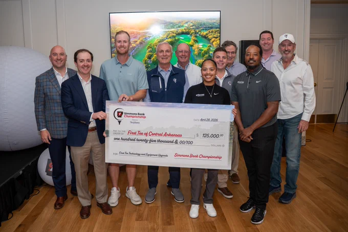 A group of people is standing indoors, holding a large check for $125,000 made out to "First Tee of Central Arkansas" from the Simmons Bank Championship. A golf course photo is displayed in the background.