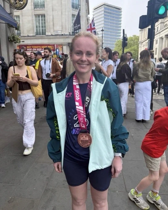 London Marathon finisher wearing a medal and jacket while standing on a busy London street after the race.