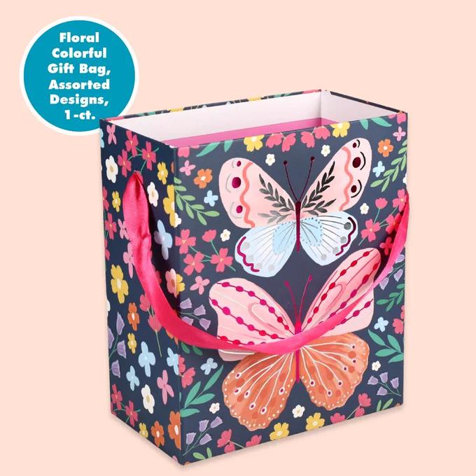 Gift bag with colorful butterfly and floral patterns on a dark background, featuring pink ribbon handles.