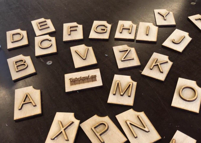 Lettres en bois gravées et découpées au laser, disposées sur une table, formant un alphabet tactile conçu pour être manipulé. 
