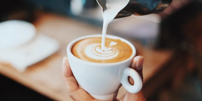 Close-up of a barista pouring steamed milk into a white cup, creating latte art in a coffee drink.