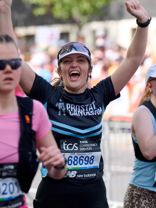 A person wearing a Prostate Cancer UK shirt and numbered bib, raising their arms in celebration during the London Marathon event.