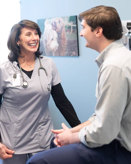 A nurse stands and smiles while talking to a patient sitting on in an exam room at Tryon Medical Partners