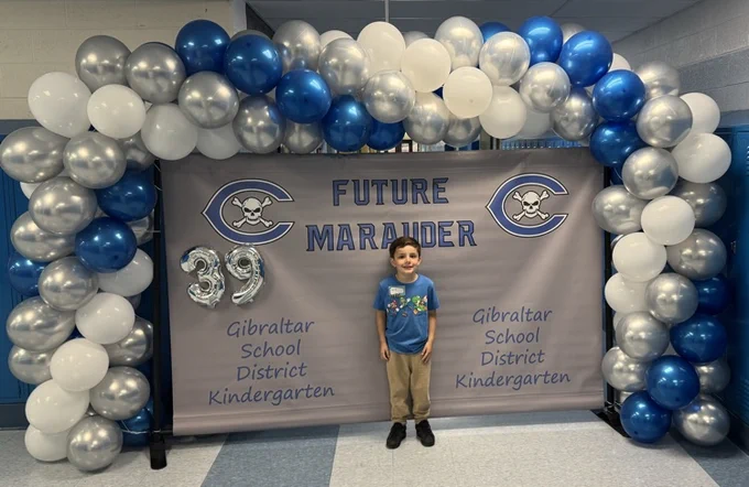 kindergarten student in front of kindergarten banner