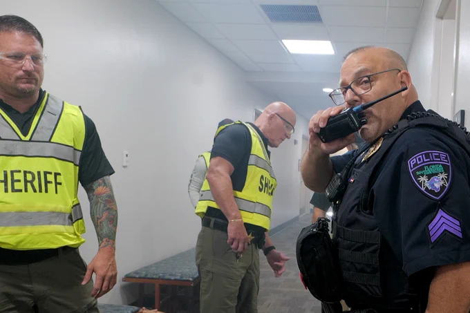 An FSW police officer talks into a handheld radio while two sheriff's officers look on during an active training in a Building A hallway on the Lee Campus.