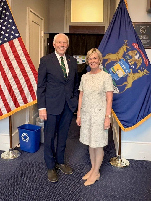 Rep Bergman and Ambassador standing in front of flags, smiling.