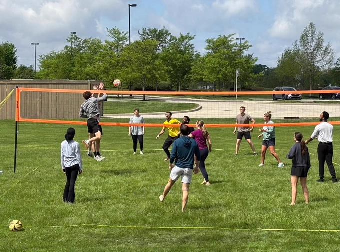 A student jumps at the net to block a volleyball during a competitive game.