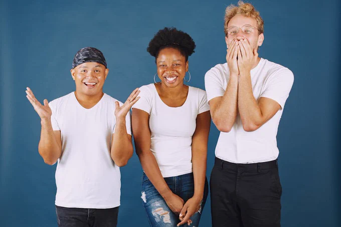 A joyful group of multicultural young adults expressing happiness against a blue background.
