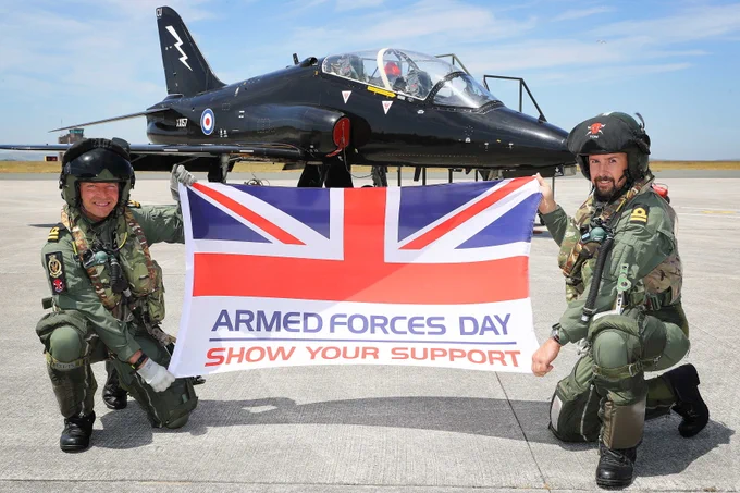 Two military personnel hold an Armed Forces Day flag that reads 'show your support'.
