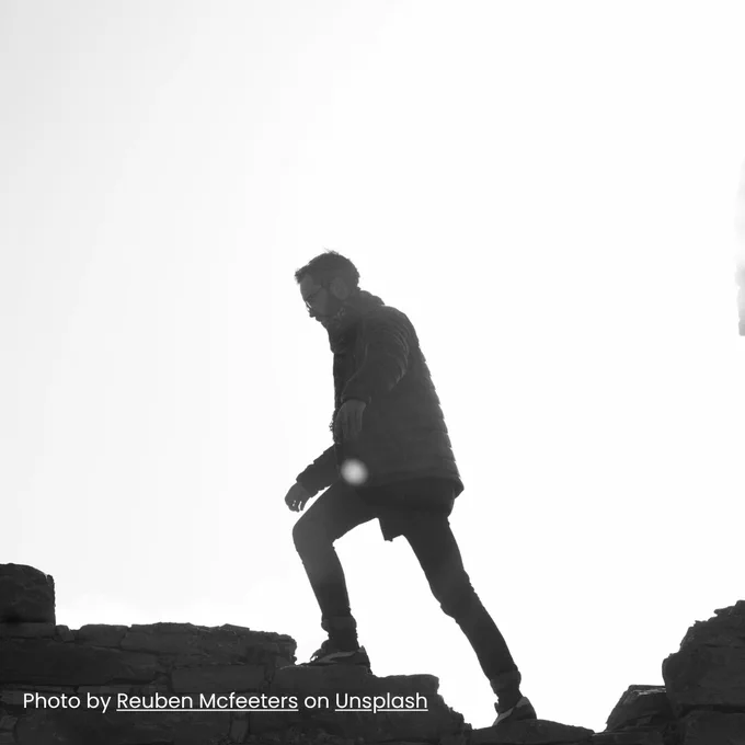 Black and white image of a man walking across rocks. Photo by Reuben Mcfeeters on Unsplash