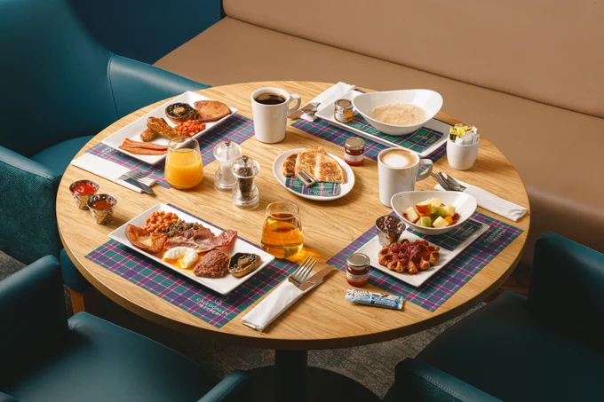 Round table set with a Scottish cooked breakfast, vegan cooked breakfast, porridge and the continental breakfast including a waffle and fruit.
